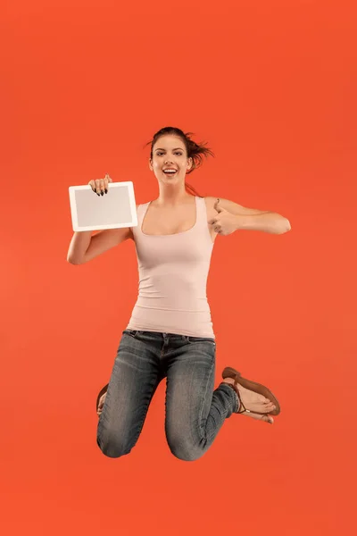 Imagen de mujer joven sobre fondo azul usando computadora portátil o tableta gadget mientras salta . — Foto de Stock