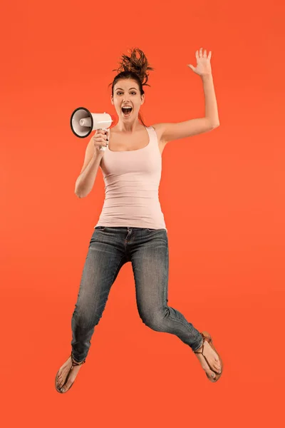 Beautiful young woman jumping with megaphone isolated over red background — Stock Photo, Image