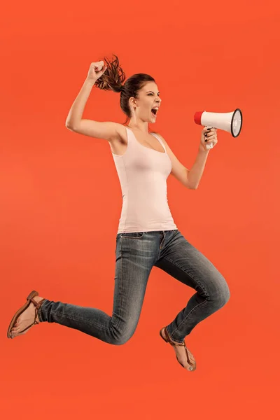 Beautiful young woman jumping with megaphone isolated over red background — Stock Photo, Image