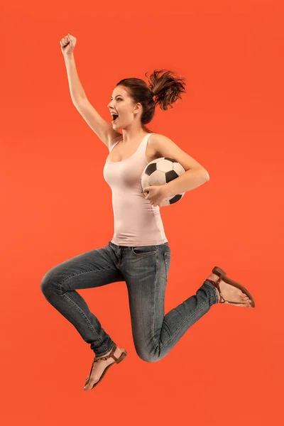 Do przodu do zwycięstwa. Młoda kobieta piłka nożna piłkarz skoki i kopiąc piłkę w studio na czerwonym — Zdjęcie stockowe