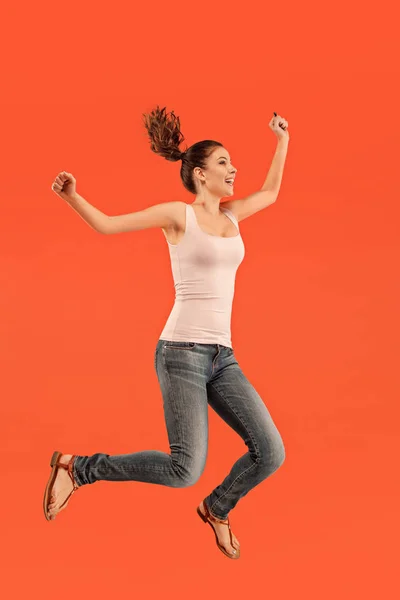 Liberdade em movimento. Mulher muito jovem pulando contra fundo laranja — Fotografia de Stock