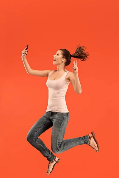 Image of young woman over blue background using laptop computer or tablet gadget while jumping.