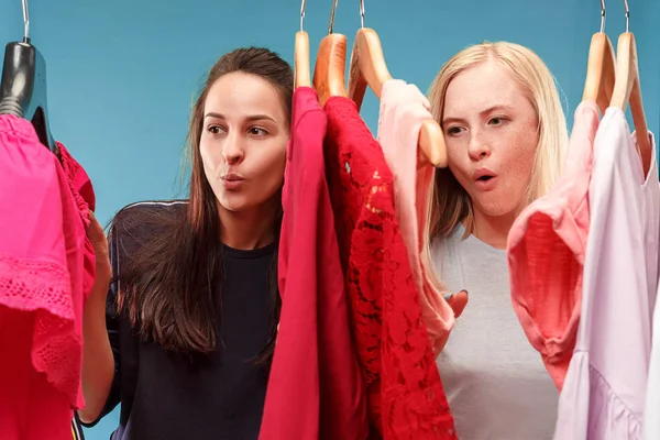 Las dos chicas guapas jóvenes mirando vestidos y probarlo al elegir en la tienda — Foto de Stock