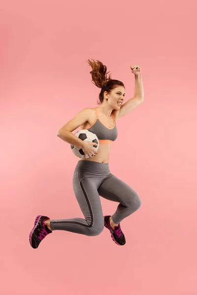 Forward to the victory.The young woman as soccer football player jumping and kicking the ball at studio on a red — Stock Photo, Image