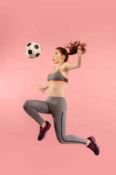 Вперед к победе. Молодая женщина, как футболист прыгает и пинает мяч в студии на красный — стоковое фото