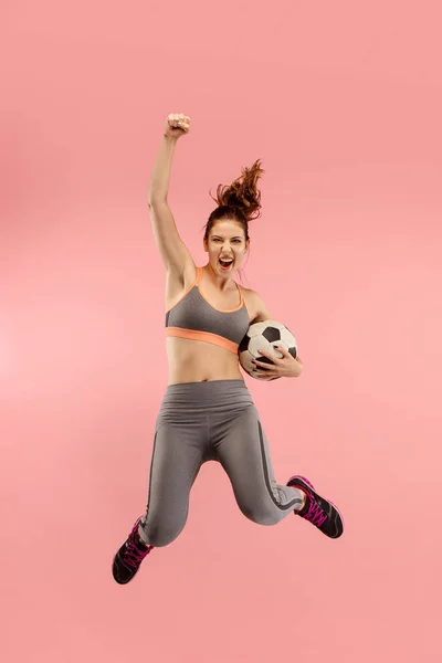 Вперед до перемоги. Молода жінка, як футболіст, стрибає і штовхає м'яч у студії на червоному — стокове фото