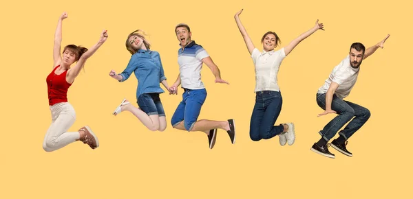 Liberdade em movimento. jovem homem e mulheres pulando contra fundo amarelo — Fotografia de Stock