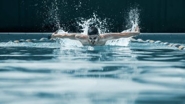 dynamic and fit swimmer in cap breathing performing the butterfly stroke clipart