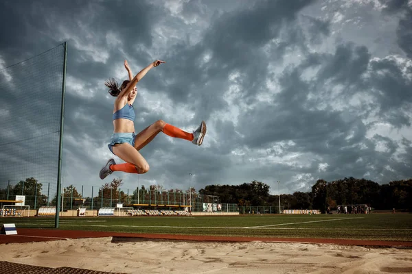 Atleta femenina realizando un salto de longitud durante una competición — Foto de Stock