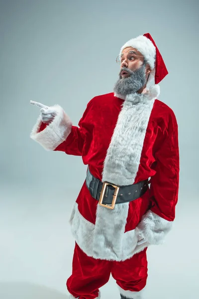 左を指しているスタジオでポーズ クリスマス帽子と変な男 年末年始 クリスマス クリスマス ギフトの概念 男は灰色のサンタ クロースの衣装を身に着けています 領域をコピーします 冬の売り上げ高 — ストック写真