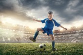 Mladý chlapec s fotbalovým míčem dělá létání kop na stadionu