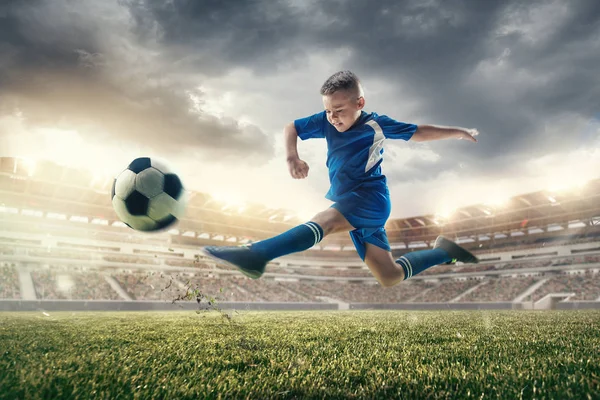 Young boy with soccer ball doing flying kick at stadium