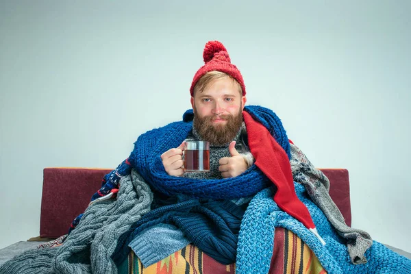 Hombre barbudo con chimenea sentado en el sofá en casa. Conceptos sanitarios . — Foto de Stock