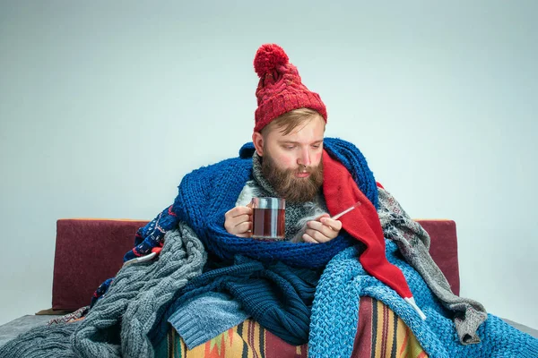 Hombre barbudo con chimenea sentado en el sofá en casa. Conceptos sanitarios . — Foto de Stock