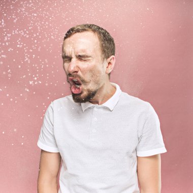Komik yakışıklı delikanlı sakal ve bıyık sprey ile sneezing ve küçük, pembe bir arka plan üzerinde stüdyo portre damla. Komik, karikatür, mizah. hastalık, enfeksiyon, ağrı. Sağlık kavramı
