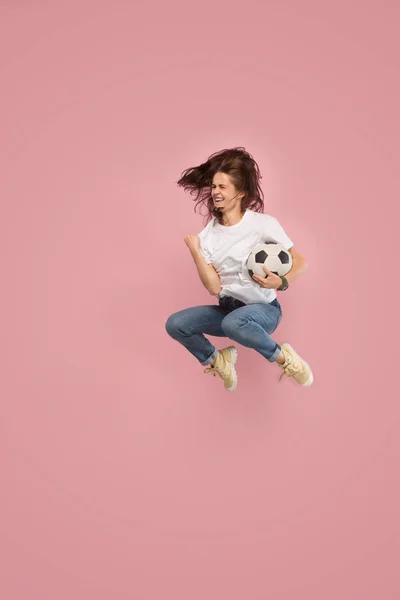 Adelante a la victoria.La joven como futbolista saltando y pateando la pelota en el estudio en rosa —  Fotos de Stock