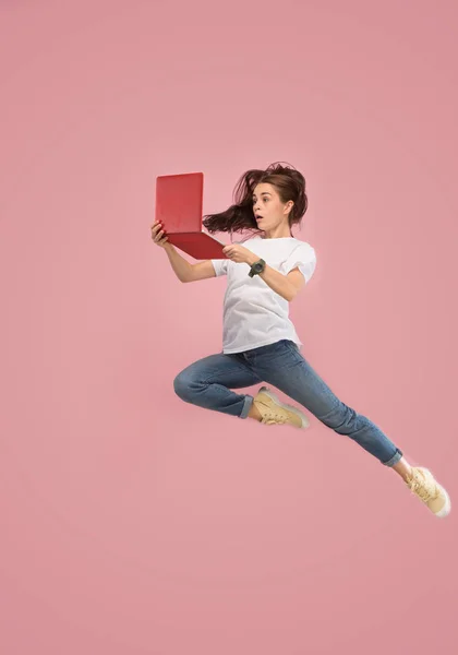 Image of young woman over pink background using laptop computer or tablet gadget while jumping. — Stock Photo, Image