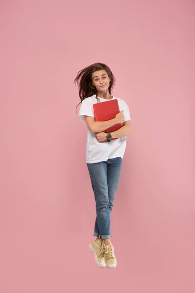 Imagen de mujer joven sobre fondo rosa usando computadora portátil o tableta gadget mientras salta . — Foto de Stock