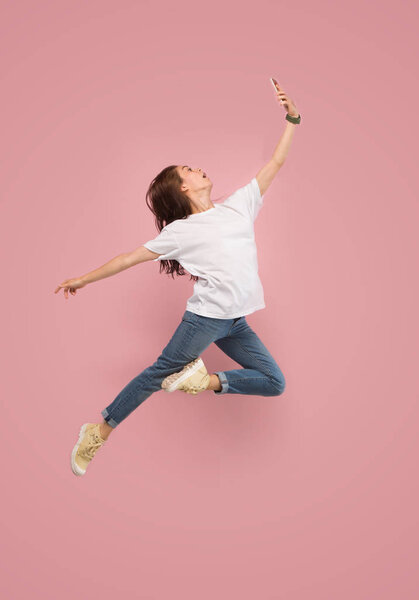 Full length of pretty young woman with mobile phone while jumping