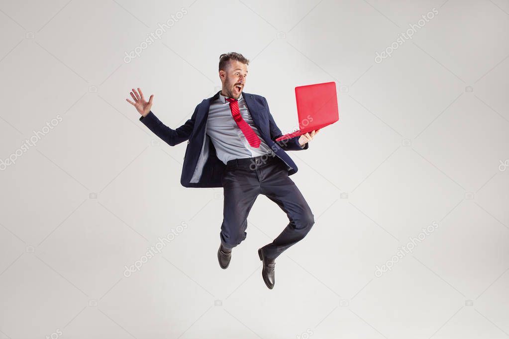 Image of young man over white background using laptop computer while jumping.