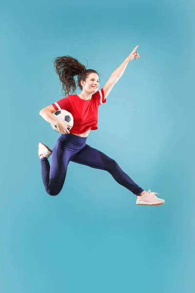 Vpřed k vítězství. Mladá žena jako fotbal fotbalový záložník skákání a kope míč ve studiu na růžové — Stock fotografie