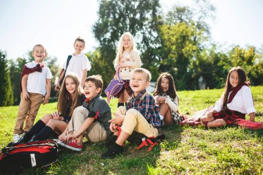 Bir grup okul ve okul öncesi yaş çocuk parkta yeşil çimenlerin üzerinde oturuyor.