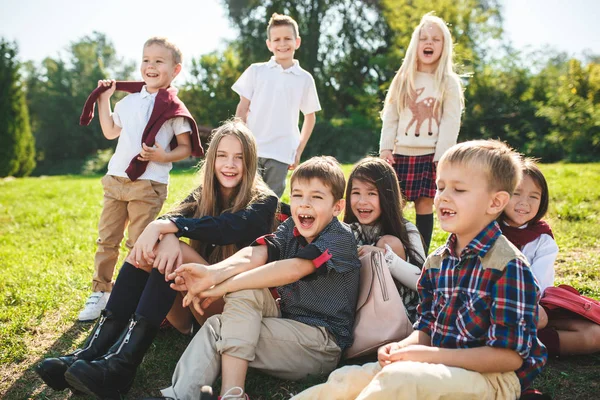 Un groupe d'enfants d'âge scolaire et préscolaire sont assis sur l'herbe verte dans le parc . — Photo