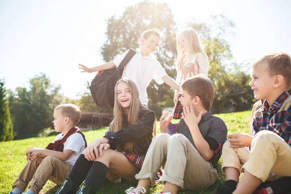 Un groupe d'enfants d'âge scolaire et préscolaire sont assis sur l'herbe verte dans le parc . — Photo