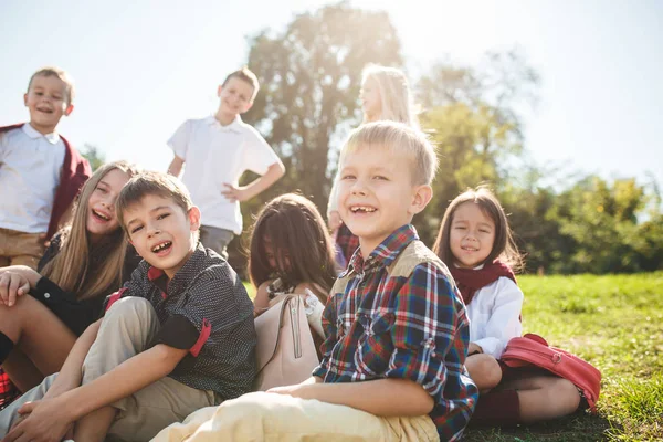 A group of children of school and preschool age are sitting on the green grass in the park. — Stock Photo, Image