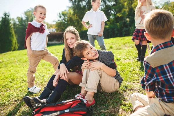 Un groupe d'enfants d'âge scolaire et préscolaire sont assis sur l'herbe verte dans le parc . — Photo