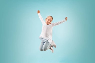 Mavi stüdyoda sevimli küçük çocuk. Kız atlama ve gülümseyen.