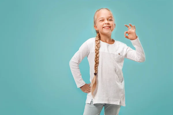 Den glada teen flicka står och ler mot blå bakgrund. — Stockfoto