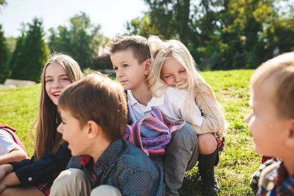 A group of children of school and preschool age are sitting on the green grass in the park. — Stock Photo, Image