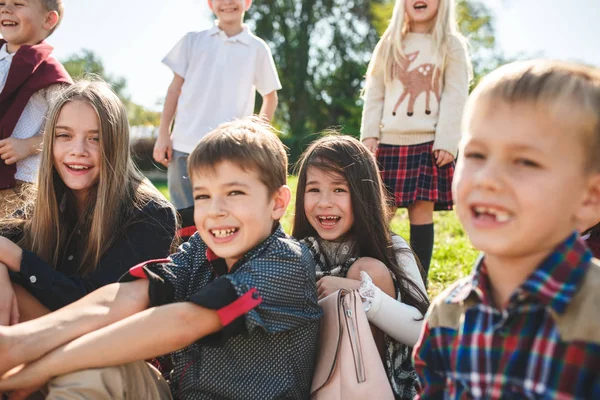 Un groupe d'enfants d'âge scolaire et préscolaire sont assis sur l'herbe verte dans le parc . — Photo