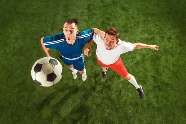 Football players tackling for the ball over green grass background