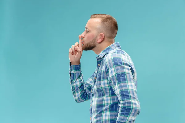 Il giovane uomo sussurrando un segreto dietro la sua mano su sfondo blu — Foto Stock