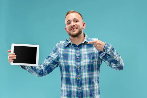 Студийное фото позитивного человека, изолированного на синем фоне, стоящего в повседневной одежде, держащего планшет и показывающего его чистый экран с счастливой улыбкой — стоковое фото