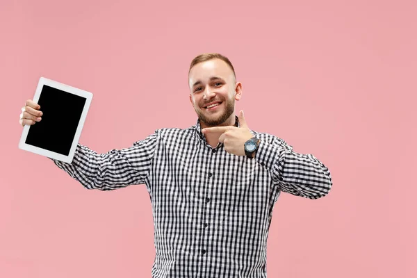 Studio bild av positiva man isolerade på rosa bakgrund står i casual kläder håller tablett och visar det tom skärm med lyckligt leende — Stockfoto