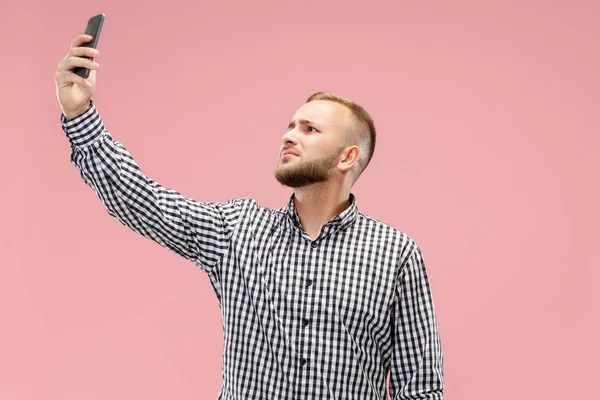 Porträtt av attraktiv ung man tar en selfie med sin smartphone. Isolerad på rosa bakgrund. — Stockfoto