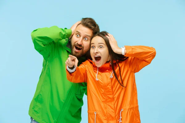 La joven pareja sorprendida posando en el estudio en chaquetas de otoño aisladas en azul — Foto de Stock