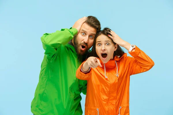 The young surprised couplel posing at studio in autumn jackets isolated on blue — Stock Photo, Image