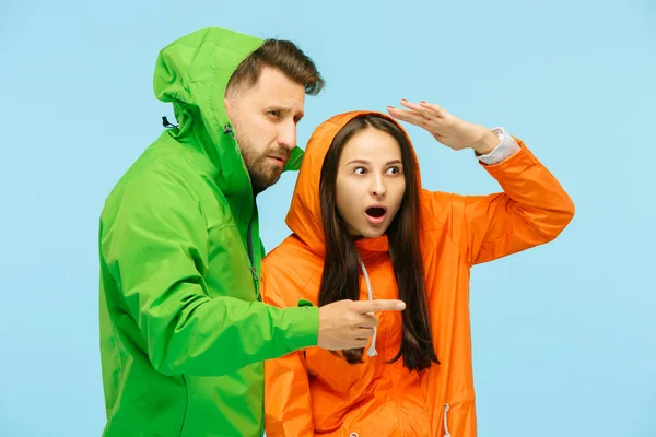 La joven pareja sorprendida posando en el estudio en chaquetas de otoño aisladas en azul — Foto de Stock