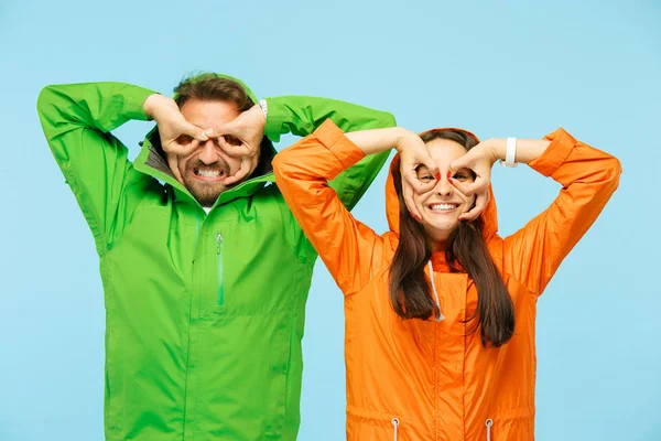 La joven pareja sorprendida posando en el estudio en chaquetas de otoño aisladas en azul — Foto de Stock