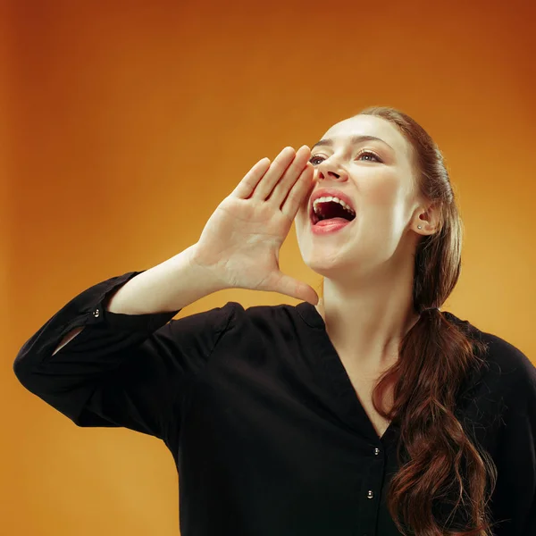 Ізольована на помаранчевій молодій випадковій жінці, що кричить на студії — стокове фото