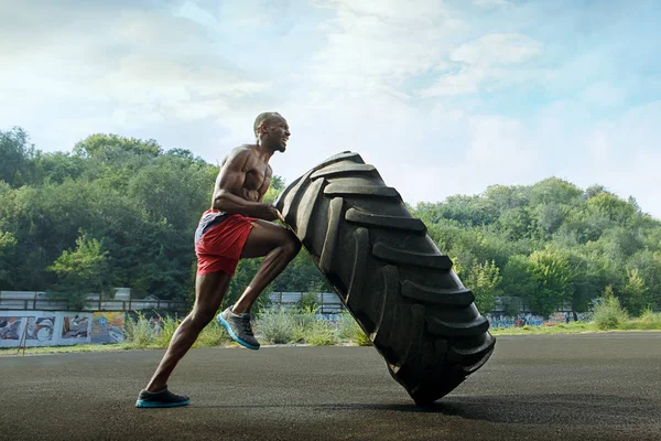 Bonito homem muscular lançando grande pneu ao ar livre . — Fotografia de Stock