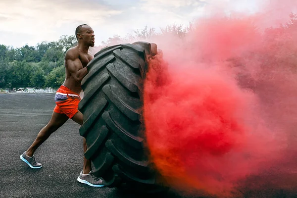Schöner muskulöser Mann dreht großen Reifen im Freien. — Stockfoto