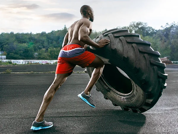 Hombre musculoso guapo volteando neumático grande al aire libre . — Foto de Stock