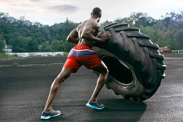 Hombre musculoso guapo volteando neumático grande al aire libre . — Foto de Stock