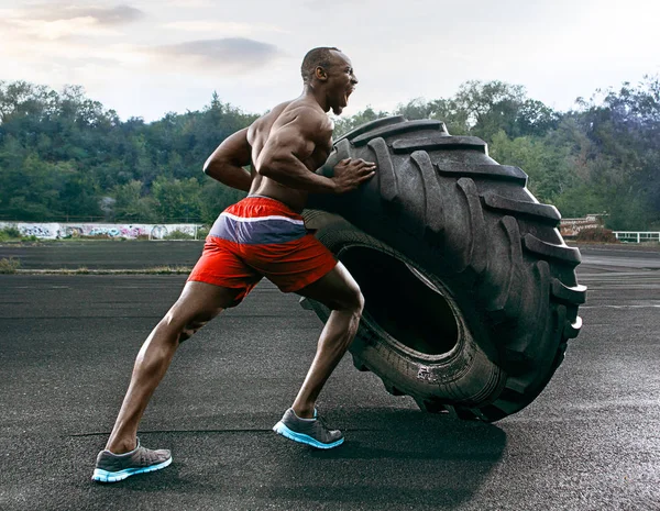Hombre musculoso guapo volteando neumático grande al aire libre . — Foto de Stock