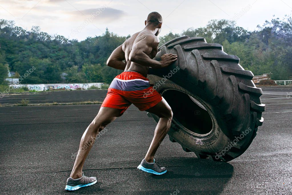 Handsome muscular man flipping big tire outdoor.